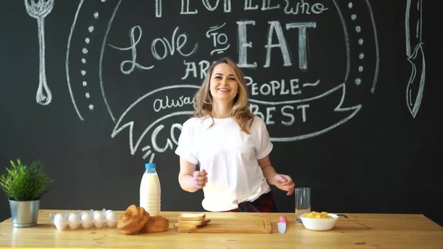 Cheerful young funny woman dancing and singing with. Cooking breakfast.