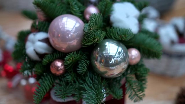 Christmas composition: pine tree branches, pink and silver christmas tree toys and cotton flower balls in gift box on plastic wrap. Craft supply for handcrafted decorations on wooden table, close-up.