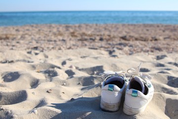 a pair of white sneakers with shoelaces abandoned on the beach