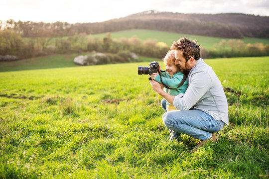A father and his toddler son with a camera outside in spring nature.