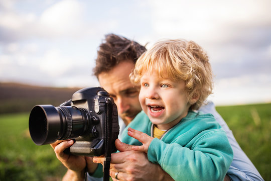 A father and his toddler son with a camera outside in spring nature.