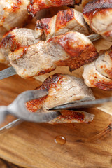 Delicious and juicy kebabs on pork skewers on a wooden board that are cut with original cutlery for meat. Still-life on a wooden background.