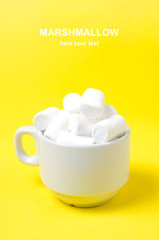 White marshmallows in a coffee mug on a bright yellow background.