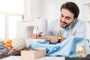 I feel alert. Content dark-haired tailor smiling and working on a sewing machine