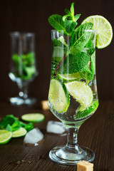 Cocktail with lime, ice, mint, on a dark wooden table, soda water