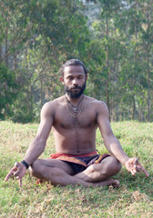 Naklejka na ściany i meble Athletic Indian man meditating in lotus yoga pose in forest