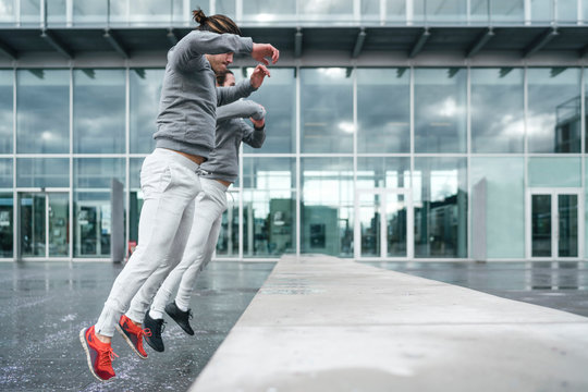 Young adult male twins training, jumping onto wall in city