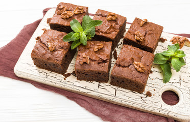 Brownie sweet chocolate dessert with walnuts and meant leaves on retro board with copy space on pastel beige background.