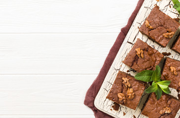 Brownie sweet chocolate dessert with walnuts and meant leaves on retro board with copy space on pastel beige background.