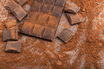 Crushed chocolate bar pieces and cocoa on gray background