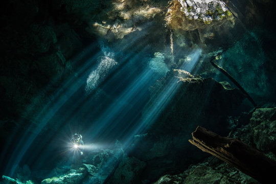 Male diver diving in underground river (cenote) with sun rays and rock formations, Tulum, Quintana Roo, Mexico