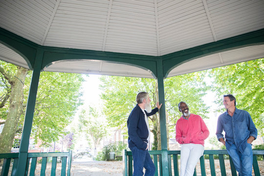 Three mature men standing under bandstand, talking