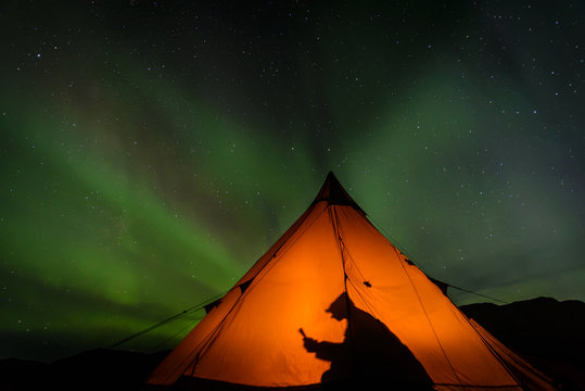 Camper reading inside tent, Aurora Borealis in background, Narsaq, Vestgronland, Greenland