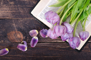 Violet tulips, petals, book on wooden background. Vintage and retro style.
