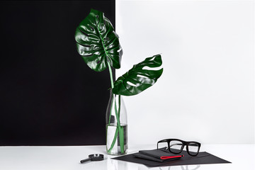 Bottle with tree leaves and glasses on table with black and white wall on background