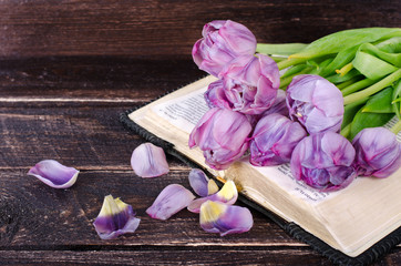 Violet tulips, petals, book on wooden background. Vintage and retro style.