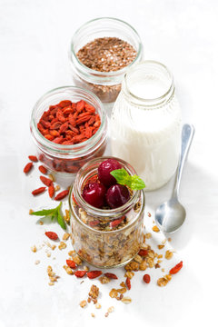 healthy food, granola with goji berries and cherries in a glass jar on white background, top view