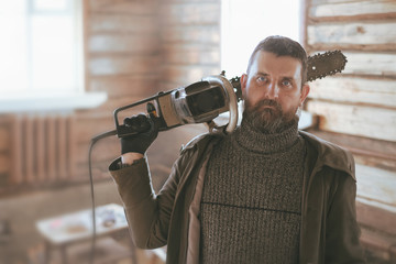 portrait of a adult man with a huge old chain saw on his shoulders in a wooden log hut