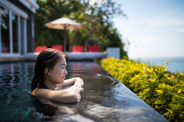Asian woman rest on edge of pool and feel relax on sunshine day, sideview