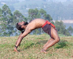 Indian man doing backband on green grass in Kerala, South India