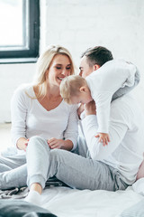 Young family playing and have fun sits on the bed. Mother, father and child. Indoor