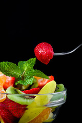 Strawberries on a spoon and assorted fruits in a bowl

