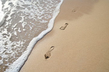 Footprints in the sand and a wave