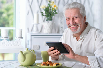 happy senior man using tablet while drinking tea at kitchen 