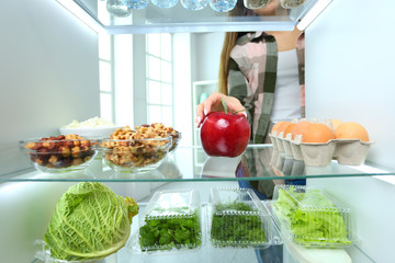 Portrait of female standing near open fridge full of healthy food, vegetables and fruits