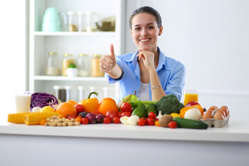 Young and cute woman sitting at the table full of fruits and vegetables in the wooden interior