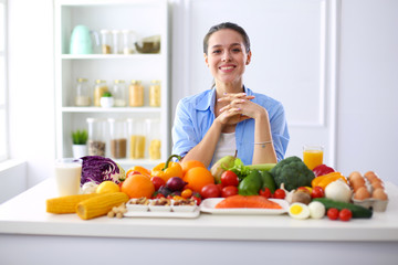 Young and cute woman sitting at the table full of fruits and vegetables in the wooden interior