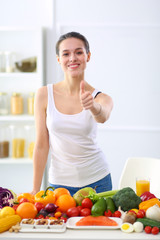 Young and cute woman sitting at the table full of fruits and vegetables in the wooden interior