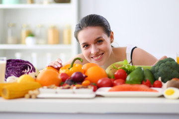 Young and cute woman sitting at the table full of fruits and vegetables in the wooden interior