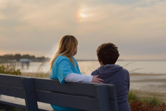 Woman And Carer Enjoying Evening Sunset By Sea