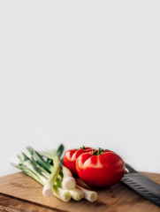 Green fresh onion and tomato on the wooden background. Copyspace.