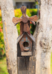 Closeup of bird wood house with gable roof and windmill in the garden