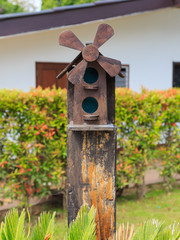 Closeup of bird wood house with gable roof and windmill in the garden
