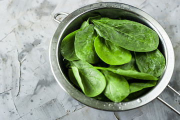 Washed spinach in a metal colander on a gray background. Fresh green leaves for cooking healthy...
