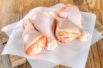 Raw chicken legs on a cutting board on an old wooden table.
