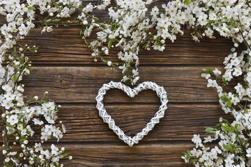 Close-up photo of Beautiful white Flowering Cherry Tree branches with white heart shape. Wedding, engagement or betrothal concept on vintage wooden background. Top view, greating card.