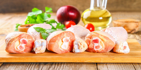 Raw chicken legs on a cutting board on an old wooden table.