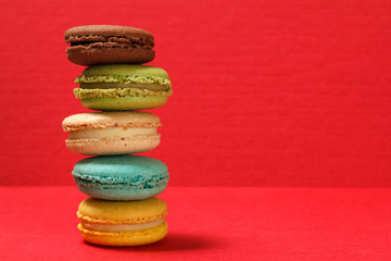 Sweet macarons cakes of different color on red textured surface