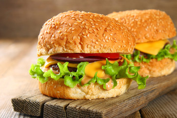 Tasty homemade burger consisting of bun, patties, salad, red onion and tomato on an old wooden table.