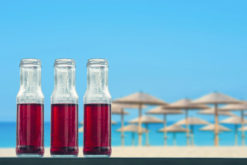 Pomegranate cold juice in bottles on the beach and straw umbrellas backgrounds 