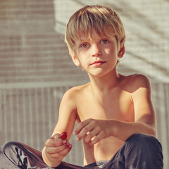 Portrait of cute happy blond boy resting outdoors, image with square aspect ratio and warm toning
