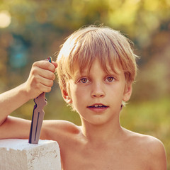 Portrait of young smiling athletic boy with throwing knife, image with square aspect ratio and warm...