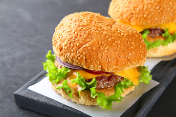 Tasty homemade burger consisting of bun, patties, salad, red onion and tomato on a dark black concrete background, table.