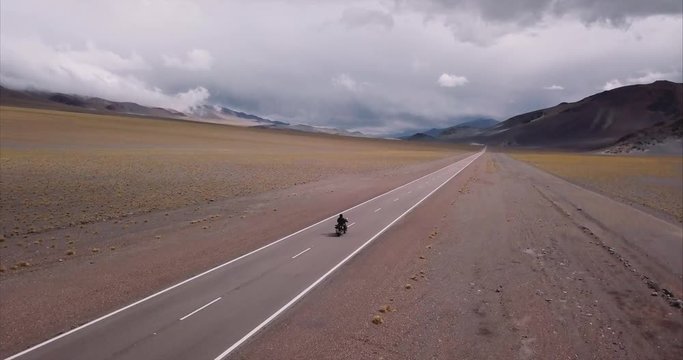 Man rides a motorcycle adventure in the straight highway of the Andean mountain range. Aerial view, 4k