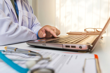doctor sitting at the table near the window in hospital and typing at laptop computer