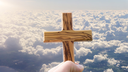 Hand hält Holzkreuz über den Wolken